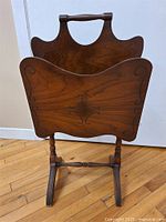 Front view of vintage wooden magazine stand showing carved detail, handle, legs and overall form