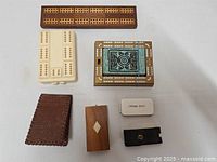Top view of the seven miniature cribbage boards and accessories arranged on a white background.