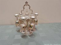 Set of six liqueur glasses hanging inverted on a detailed ornate silverplate holder with embossed floral patterns.