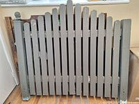 Front view of vintage wooden garden fence with grey vertical slats and rounded tops, showing chipping paint and wear.