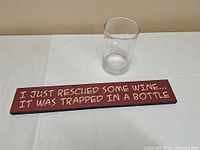 Photo of a rectangular wooden sign, 24 inches wide, deep red with white handwritten text about wine rescue.