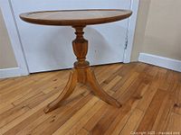 Full view of round wooden table showing top and pedestal leg with three feet