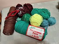 Photo showing multiple balls and skeins of assorted wool yarn in various colors and types including green, yellow, blue, maroon, and brown cone.