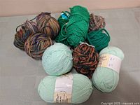 Photo showing eight skeins of wool yarn in various colors including mint green, solid green, brown multicolor blends and tan variegated.