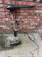 Full view of the black electric trolling motor showing propeller, shaft, and cables extended on concrete against brick wall
