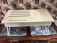 Front view of adjustable laptop/serving table in light wood with white metal legs unfolded, showing slatted portion and drawer handle.