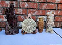 Front view showing entire lot including dark hardwood fisherman figurine, circular carved incense holder on stand, carved soapstone bud vase, and resin small vase.