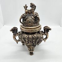 Front view of incense burner showing tripod base, dragon handles, lid with lion finial.