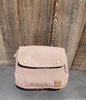 Front view of the light beige canvas bike handlebar bag with two brass snap buttons and a small MEC logo patch.