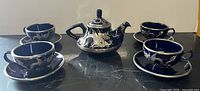 Front view of blue ceramic and metal dragon tea set showing teapot, four teacups, and saucers