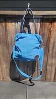 Blue canvas purse hanging outdoors showing full front view with shoulder and longer strap.