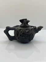 Side view showing the handle shaped like a branch, with bamboo stalks and flower relief on the body and lid of the clay teapot.