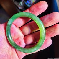 Hand holding dark green jade bangle showing color and material details.