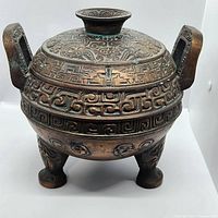 Front view of large Asian metal incense burner showing geometric and dragon patterns with two square handles and tripod legs.