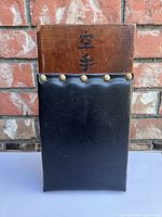 Front view of makiwara board showing black leather striking pad with brass studs and Japanese kanji characters on wood.