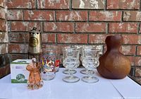 Front view of all vintage glass collectibles including Disney Fantasia McDonald's glass, McPizza glass cup, antique Eccles lamp, blown glass perfume bottle, amber vase, and Kings Crown goblets set, displayed against brick wall.
