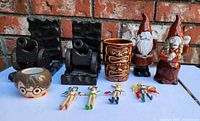 Lot overview showing Harry Potter mini ceramic cup, zombie gnome figurines, vintage Sailor Moon keychains, tiki mug and wooden cannon bookends on outdoor surface with brick background.