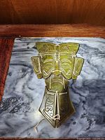 Front view of the carved jade mask placed on a marble surface, showing detailed face carving and string connectors.