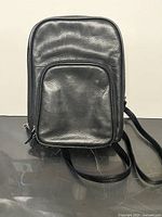 Front view of compact black leather mini backpack showing front zippered pocket and main compartment.