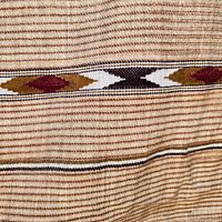 Close-up of the textile showing the horizontal decorative diamond pattern band with colors black, white, burgundy, mustard on brown and beige striped wool fabric.
