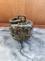 Front view of carved stone container placed on marble surface with wooden background.