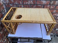 Side view showing bamboo and rattan construction, circular cut out for cup holder, and magazine rack on one side with woven bamboo surface.