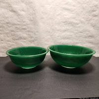 Two hunter green vintage Pyrex nesting bowls side by side, showing color and shape.