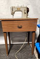 Front view of Pfaff sewing machine mounted into wooden cabinet showing overall condition and size relative to floor.