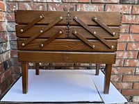 Front view of a vintage wooden sewing box with legs showing expandable upper compartments.