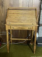Front view of vintage oak small roll top secretary desk showing the roll top closed and one drawer with brass knobs below