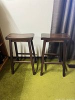 Two dark brown wooden stools side by side, showcasing overall condition and structure including legs and seats.