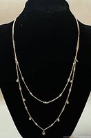 Front view of the two-strand silver necklace displayed on black bust showing dangling bead details.