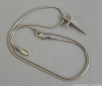 Photo of full silver necklace laid out on surface showing cross pendant and chain with clasp.