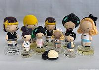 Front view of all nine Harajuku Lovers G by Gwen Stefani perfume bottles arranged in two rows showing doll-shaped caps and glass bases containing perfume liquid.