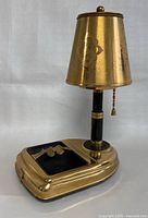 Front diagonal view showing the lamp shade, brass body, and black ashtray with gold cigarette rests.