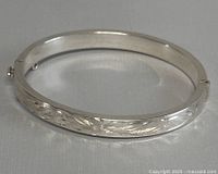 Front view of silver bangle showing engraved floral or leaf pattern and hinge detail