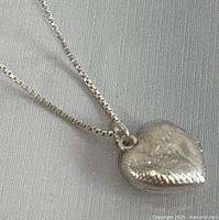 Close-up of heart-shaped sterling silver locket pendant, showing engraved design.