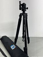 Full view of Cameron T200BH tripod standing fully extended next to its original carrying case lying on table.