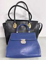Front view of black Cole Haan handbag with double handles and blue DAKS handbag placed in front of it to show size difference.