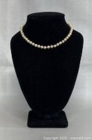 Pearl necklace displayed on black velvet stand showing full necklace arrangement.