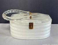 Front angled view of lucite handbag showing frosted white ribbed base, clear handle and metal latch.