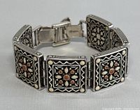 Silver-tone signed Brighton bracelet laid out as a loop, showing multiple connected square links with floral patterns and colored inset accents.