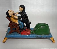 Side view of the vintage cast iron dentist and patient mechanical coin bank showing detailed figures and chair.
