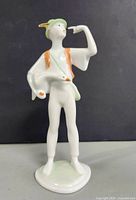 Front view of the figurine showing the boy with a green hat, orange vest, and holding a white goose at his side.