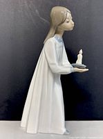 Full side view of the porcelain figurine showing the girl in white gown holding a candle and dish.