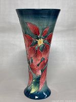Front view of the vase showing vibrant red leaves and yellow flower centers on a deep blue-green gradient background.