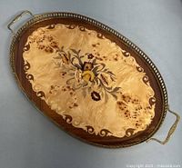 Oval wooden tray top-down view displaying intarsia marquetry floral design and brass handles, showing condition and size.