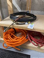 Three air hoses on wooden shelving: black coiled hose on top and orange and red hoses below.