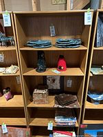 Front view of bookshelf showing five shelves containing some plates, fabric items, books, and small decorative objects on some shelves (contents not included in sale). Shelf has occupant tag 246 attached.