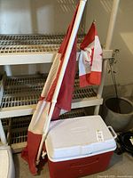 Rubbermaid cooler with white lid and Canadian flag on white pole resting nearby on floor.